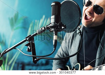 Close Up Of A Man Singer Sitting On A Stool In A Headphones With A Guitar Recording A Track In A Hom