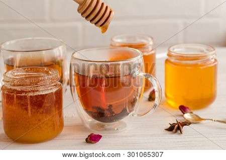 A Viscous Stream Of Sweet Amber Flower Honey Flows From A Wooden Honey Spoon Into A Glass Cup Of Tea
