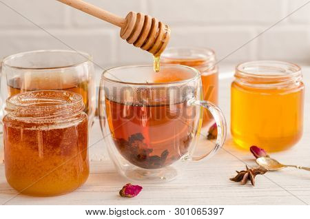 A Viscous Stream Of Sweet Amber Flower Honey Flows From A Wooden Honey Spoon Into A Glass Cup Of Tea