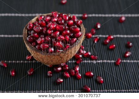 Garnet Seeds In Coconut Shell In Black Wood Background