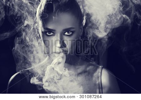 Woman Smoking Vape And Exhaling Smoke In Studio, Black And White Shot