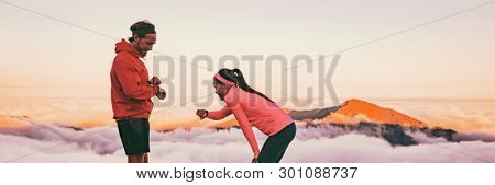 Runners tired breathing after training looking at their wearable tech sports watch checking heart rate health data. Two athletes couple running together in outdoors mountain banner panorama.