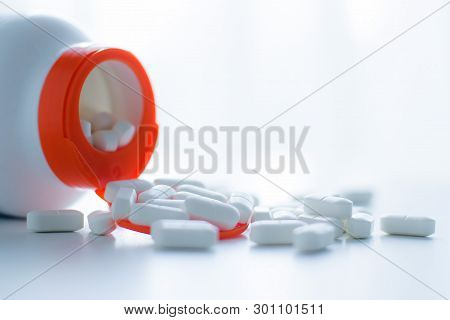White Tablets Spilling Out Of A Plastic White Bottle With A Tablet