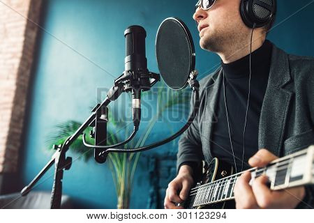 Close Up Of A Man Singer Sitting On A Stool In A Headphones With A Guitar Recording A Track In A Hom