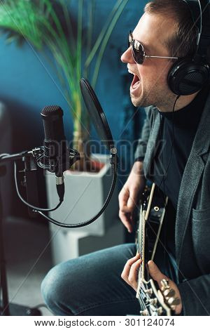 Close Up Of A Man Singer Sitting On A Stool In A Headphones With A Guitar Recording A Track In A Hom