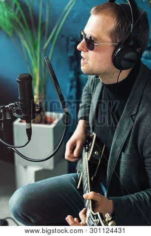 Close Up Of A Man Singer Sitting On A Stool In A Headphones With A Guitar Recording A Track In A Hom