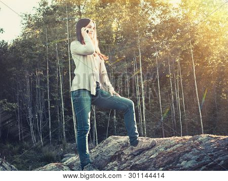 Young Pretty Girl Smiles And Talks On The Phone While Standing On A Large Stone
