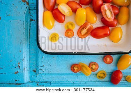 Small Cherry Tomatoes, Red And Yellow, In An Enameled Baking Sheet On A Blue Background, Top View