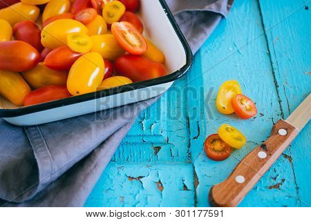 Small Cherry Tomatoes, Red And Yellow, In An Enameled Baking Sheet On A Blue Background