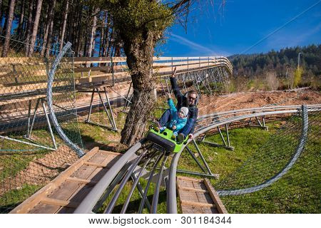 Excited young father and son driving on alpine coaster while enjoying beautiful sunny day in the nature