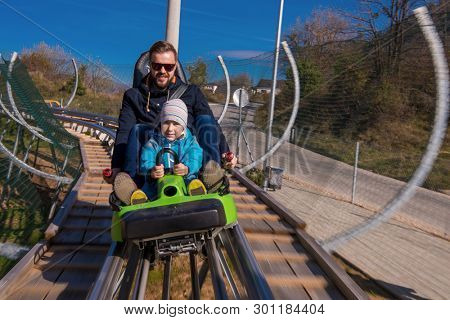 Excited young father and son driving on alpine coaster while enjoying beautiful sunny day in the nature