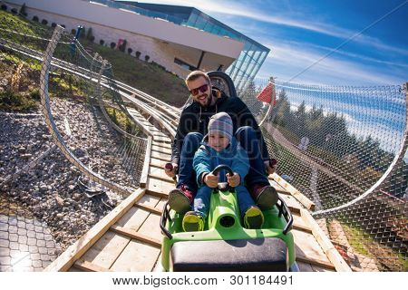 Excited young father and son driving on alpine coaster while enjoying beautiful sunny day in the nature