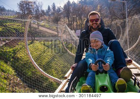 Excited young father and son driving on alpine coaster while enjoying beautiful sunny day in the nature