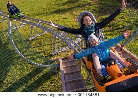 Excited young mother and son driving on alpine coaster while enjoying beautiful sunny day in the nature