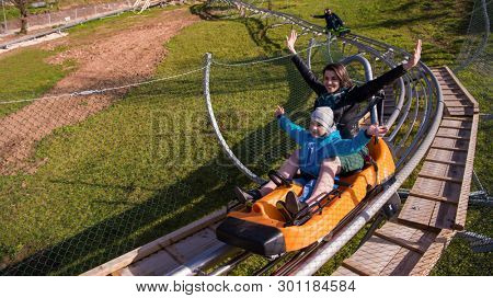 Excited young mother and son driving on alpine coaster while enjoying beautiful sunny day in the nature