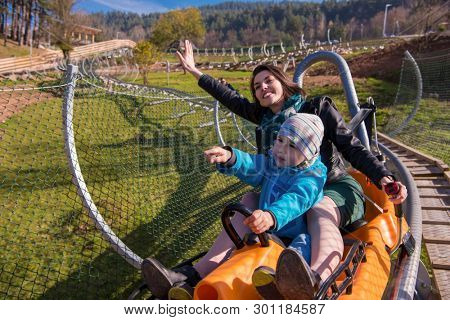 Excited young mother and son driving on alpine coaster while enjoying beautiful sunny day in the nature