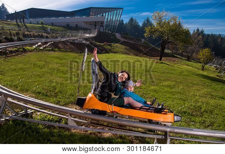 Excited young mother and son driving on alpine coaster while enjoying beautiful sunny day in the nature
