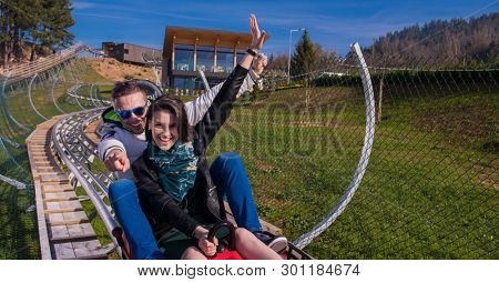 Excited young couple driving alpine coaster while enjoying beautiful sunny day in the nature