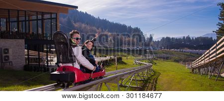 Excited young couple driving alpine coaster while enjoying beautiful sunny day in the nature