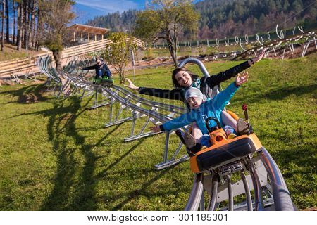 Excited young mother and son driving on alpine coaster while enjoying beautiful sunny day in the nature
