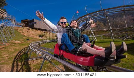 Excited young couple driving alpine coaster while enjoying beautiful sunny day in the nature