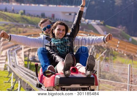 Excited young couple driving alpine coaster while enjoying beautiful sunny day in the nature