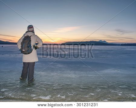 Traveler Stay On Ice Of Frozen Sea. Woman With Backpack And Long Warm Jacket. Footprints In Ice Of L