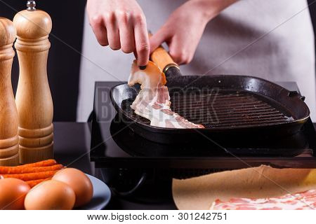 Young Woman In A Gray Apron Fries Bacon