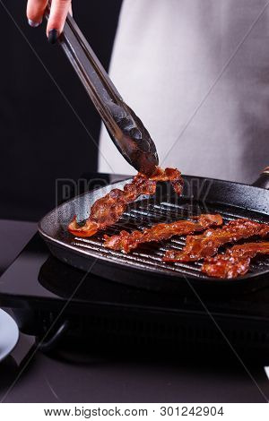 Young Woman In A Gray Apron Fries Bacon