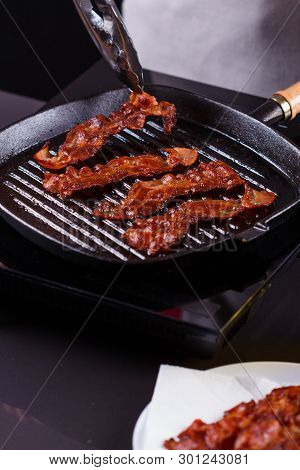Young Woman In A Gray Apron Fries Bacon