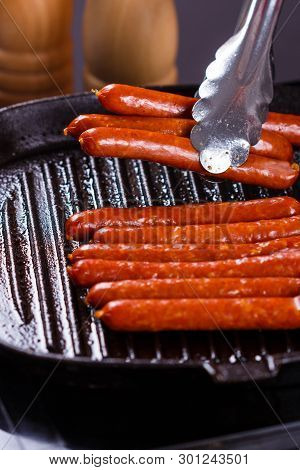 Young Woman In A Gray Apron Fries Sausages
