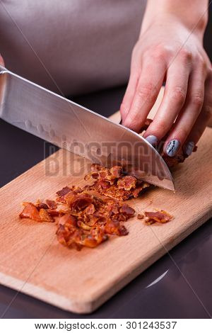 Young Woman In A Gray Apron Cuts Roasted Bacon