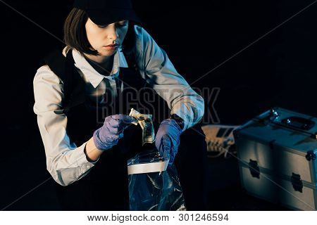 Investigator In Uniform Putting Dollar Banknote In Ziploc Bag Isolated On Black