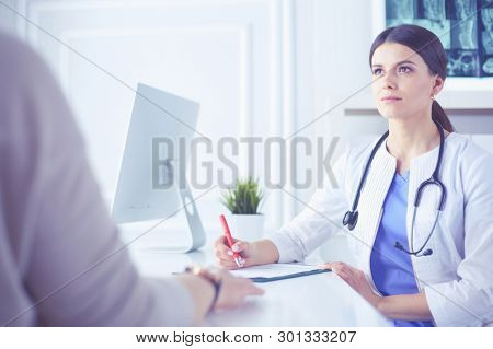Doctor and patient discussing medical problems in a hospital consulting room. Doc filling in a patient's form