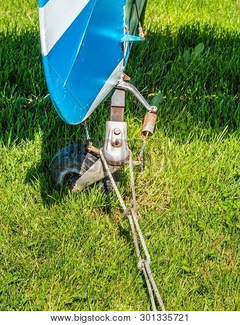 Rear View Of Tail Rudder And Wheel Of A Vintage Aircraft Parked On A Grass Field.