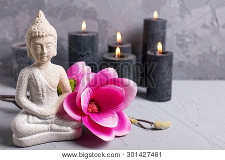 Buddha, Black Burning Candles And Pink Magnolia Flowers On Grey Textured Background. Spa Or Still Li