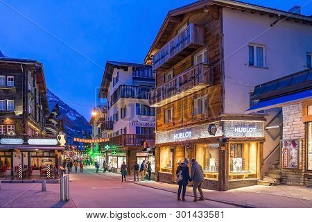 Zermatt, Switzerland - April 11, 2018: Tourists At Street View Of Old Town Zermatt In Twilight Time 