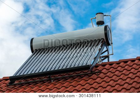 Solar Water Heater Boiler On Residentual House Rooftop, Blue Sky With White Clouds Background.
