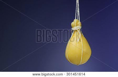 Typical Italian Cheese Caciocavallo Ripens In Ropes In A Hanging State On Blue Background.