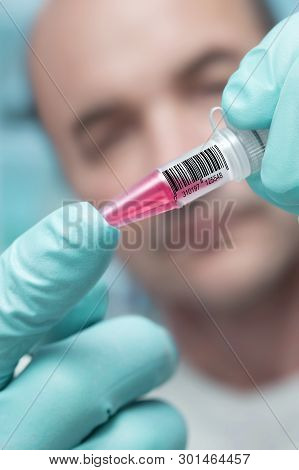 Scientist Or Tech Holds Liquid Biological Sample With Bar Code In Gloved Hands.