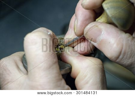 The Master Jeweler Holds The Working Tool In His Hands And Makes Jewelery At His Workplace