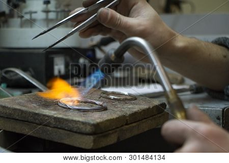 The Master Jeweler Holds The Working Tool In His Hands And Makes Jewelery At His Workplace