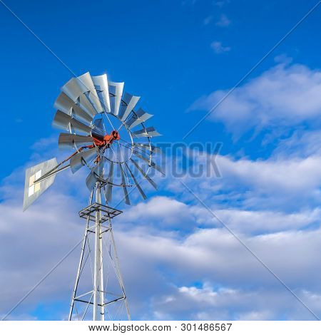 Clear Square Shiny Steel Windpump Against A Vibrant Blue Sky With Cottony Clouds