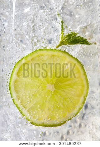 Fresh mint leaf and a slice of lime with bubbles in a glass with ice. Macro photo of refreshing drink