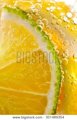 Macro photo of yellow lemon slices and lime with lots of bubbles in a glass with water. Summer refreshing cocktail