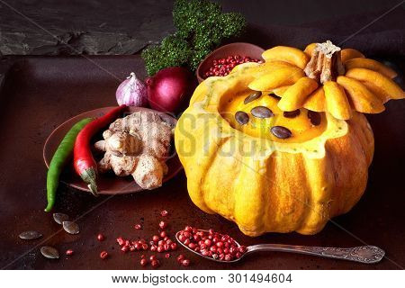 Spicy Pumpkin Soup Served In A Hollowed Pumpin On Dark Background. The Soup Was Seasoned With Chili,