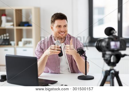 blogging, videoblog and people concept - male blogger with camera recording video review of wireless microphone showing thumbs up gesture at home office