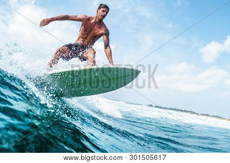 HIMMAFUSHI / MALDIVES - MARCH 10, 2019: Young surfer with lean muscular body rides the tropical wave