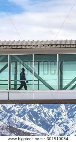 Clear Vertical Silhouette Of A Man Walking Inside A Skybridge Connecting Buildings