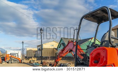 Panorama Red Excavator On A Construction Site For New Homes Against Cloudy Blue Sky